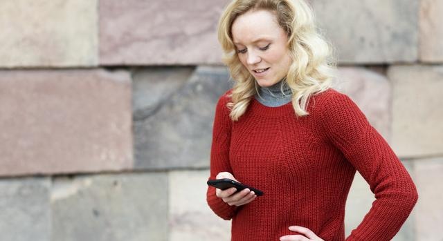 En kvinna i röd tröja tar emot ett sms innehållande driftinformation