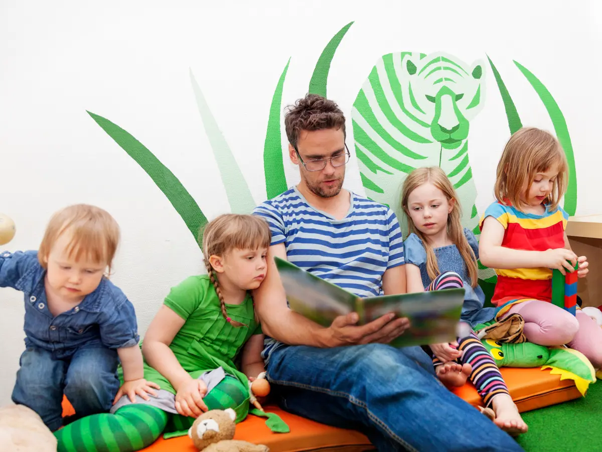 Barn som sitter intill en kille som läser i en bok.