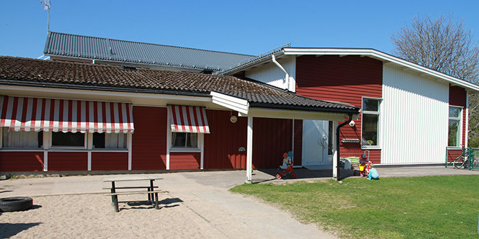 Bild på förskola Solrosen, vitt och rött hus med gräsmatta framför