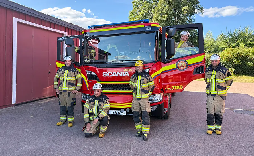 Brandmän stående framför och i en röd brandbil.